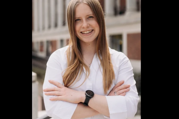 Auria Lee, fair-skinned with long straight blonde hair, smiling in a white button-down shirt.