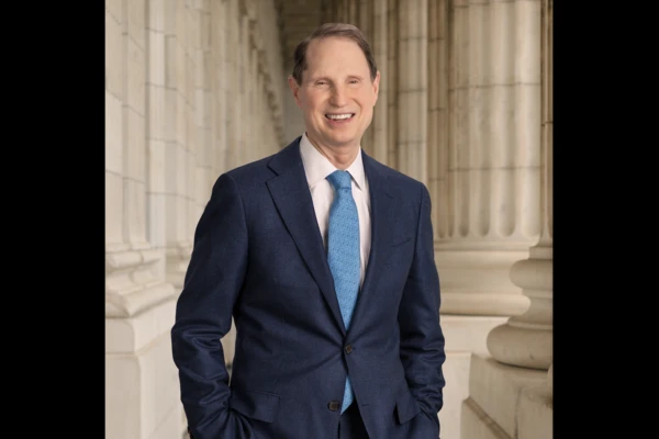 U.S. Sen. Ron Wyden, standing in a navy blue suit in front of marble columns.
