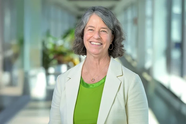 Debbie Craig, middle-aged white woman in white blazer and green blouse, smiles in a well-lit hallway.