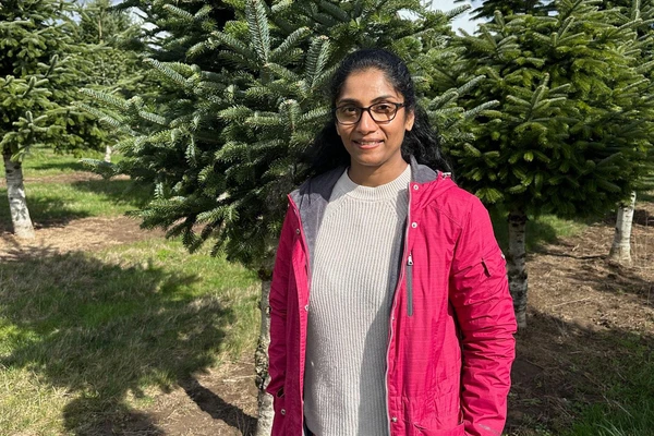 Priya Rajarapu in a bright pink jacket standing in front of Christmas trees. 