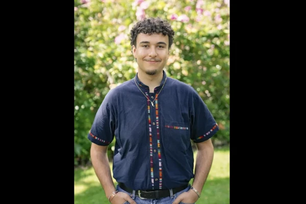 Donovan Morales poses in a blue short-sleeved button-down shirt with hands in his pants pockets.