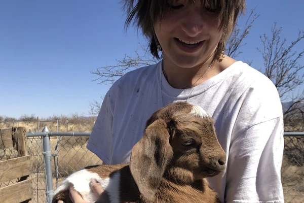 Frances Jensen looks down at a very cute baby goat in their arms.
