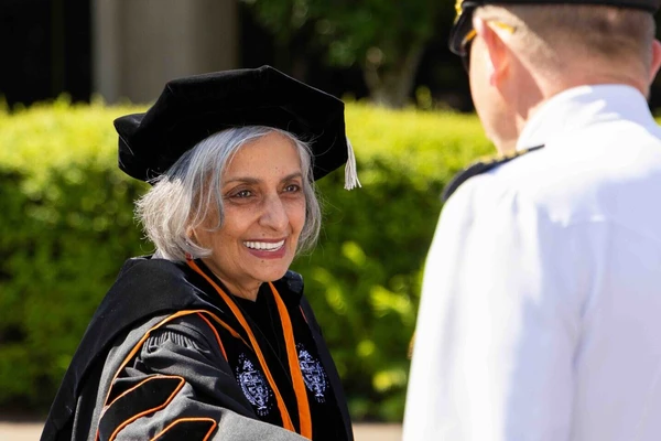 President Murthy in her graduation robe, hood and fancy Ph.D. hat smiles and greets a man.