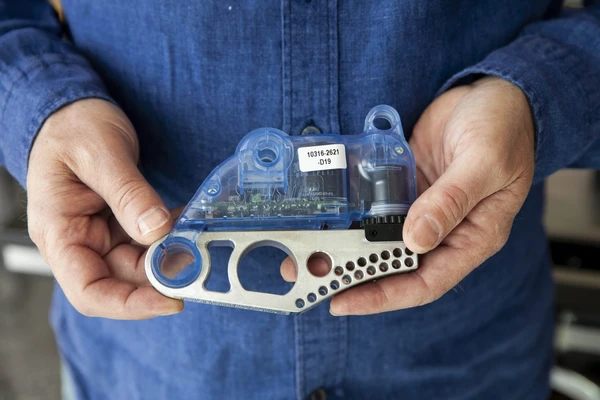 Close-up of a man's hands holding a small metal gadget, the piece that makes the SawStop blade stop as soon as it hits flesh.