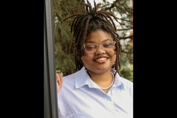 Headshot of Ph.D. student Anitra Higgins, a Black woman wearing locs, glasses and a light-blue collared shirt.
