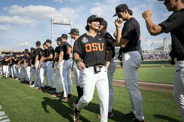 OSU baseball players in black baseball shirts and tight white pants stand in a line and high-five each other.