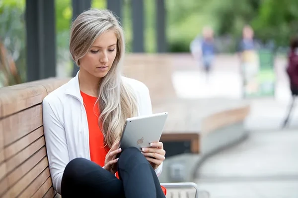 Blonde girl on a bench reads her iPad.