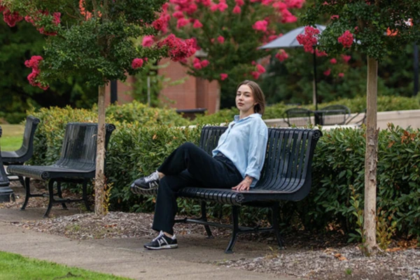 Zlata Goleva sits on a metal bench with bright pink crape myrtle trees in the background.