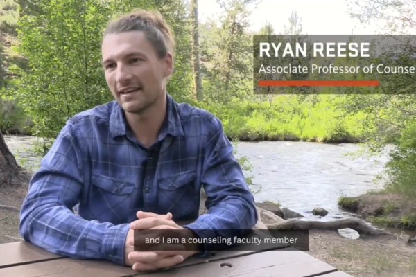 Ryan Reese wearing a flannel shirt sitting at an outdoor picnic table.