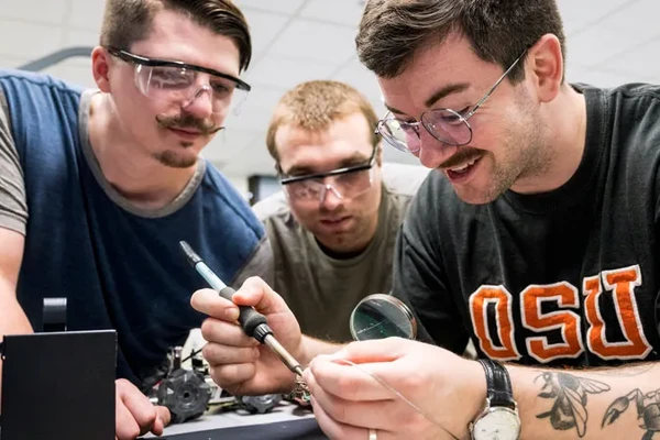 Three men gather excitedly around a welding tool.