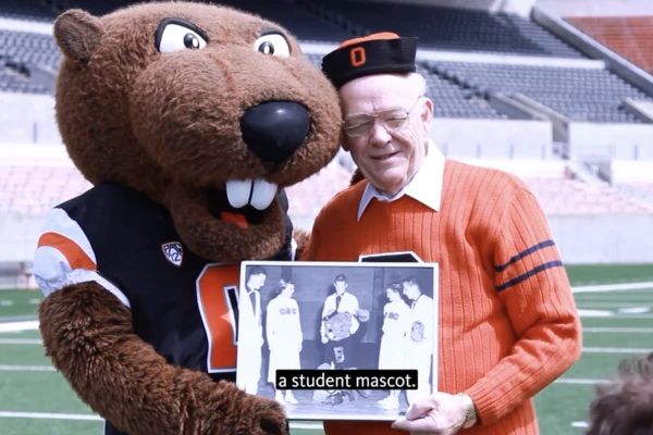 The Benny Beaver mascot standing next to an elderly man in an orange sweater, who was the first person to embody Benny.
