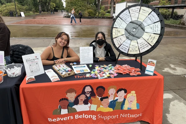 Two students sitting at a Beavers Belong Support Network table during an outdoor tabling event.