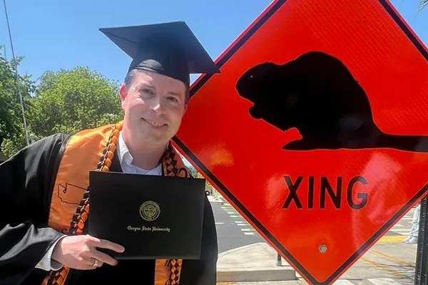 Graduate in front of beaver crossing sign