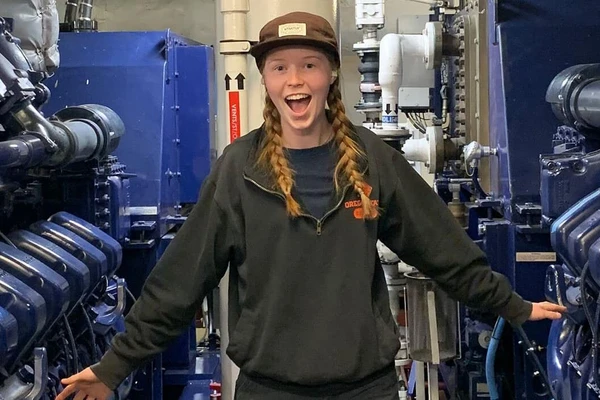 Maya Moran in braids and a baseball cap smiling while surrounded by marine gear.