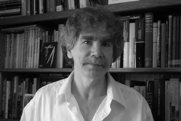 Black-and-white photo of writer and professor Tracy Daugherty in front of his bookshelves.