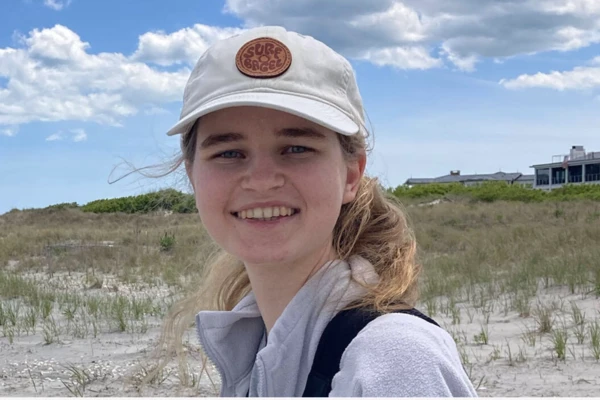 A young blonde woman in a baseball cap smiling on a sand dune.