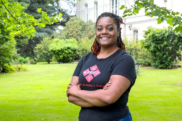 A young Black woman poses outdoors, smiling with her arms crossed.
