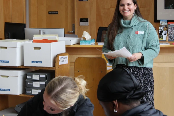 Archivist Natalia Fernandez looks on as students examine documents from archive boxes.