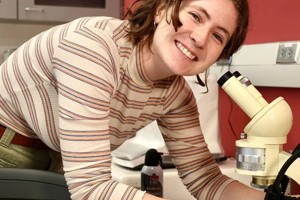 Cadence Russell leaning over a microscope and smiling for the camera.