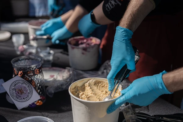 Blue-gloved hands scoop ice cream out of a white carton.